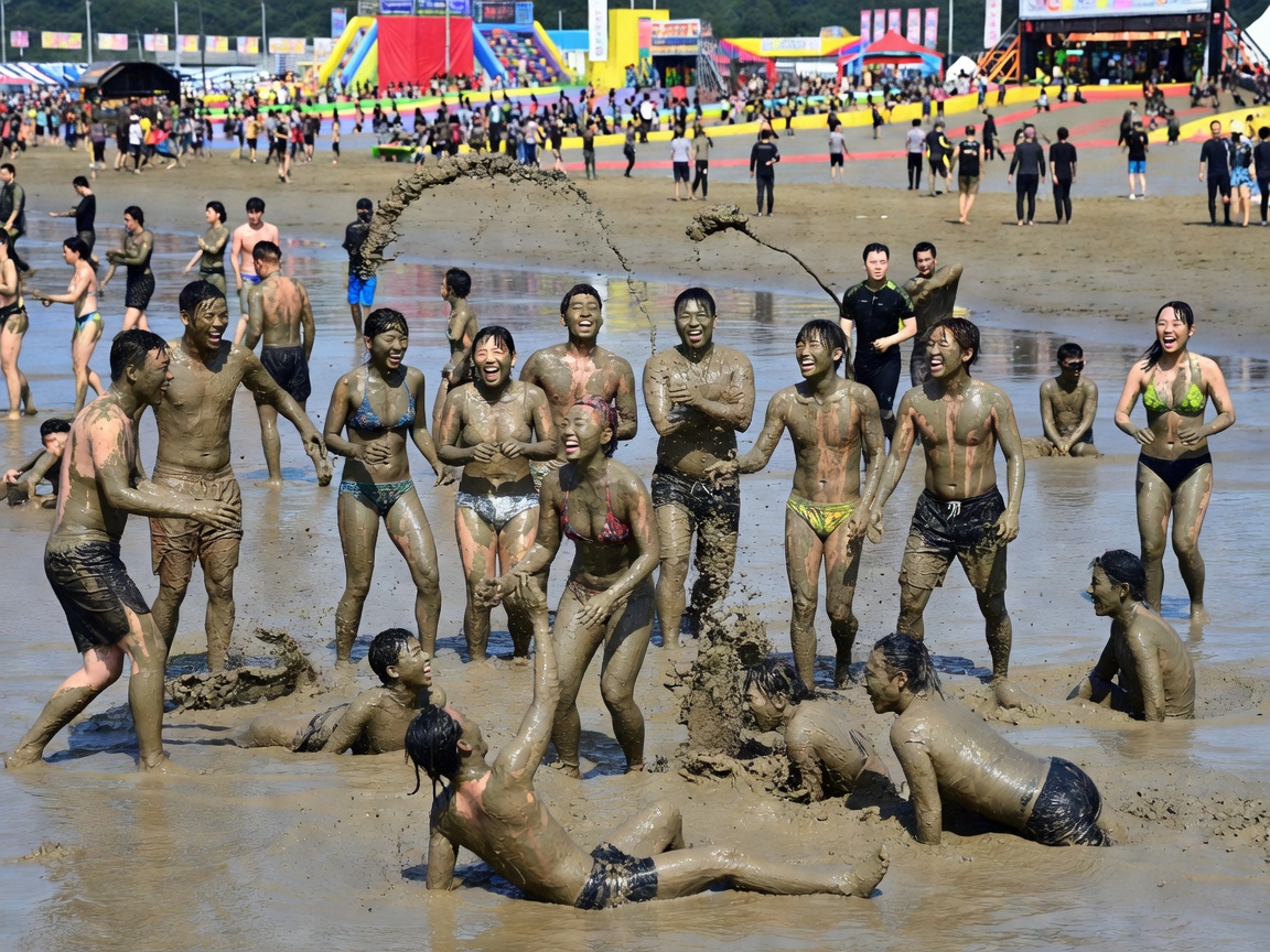 People covered in therapeutic mineral mud sliding and celebrating on beach